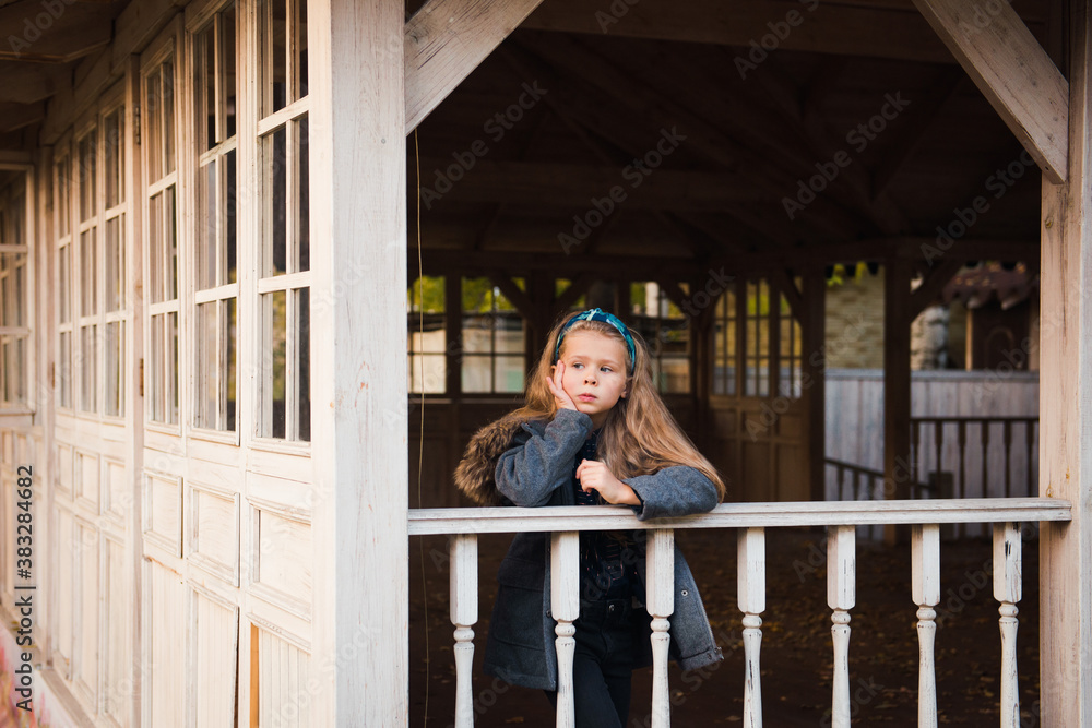 Fashion 8 y.o. girl posing on empty wooden terrace in autumn park
