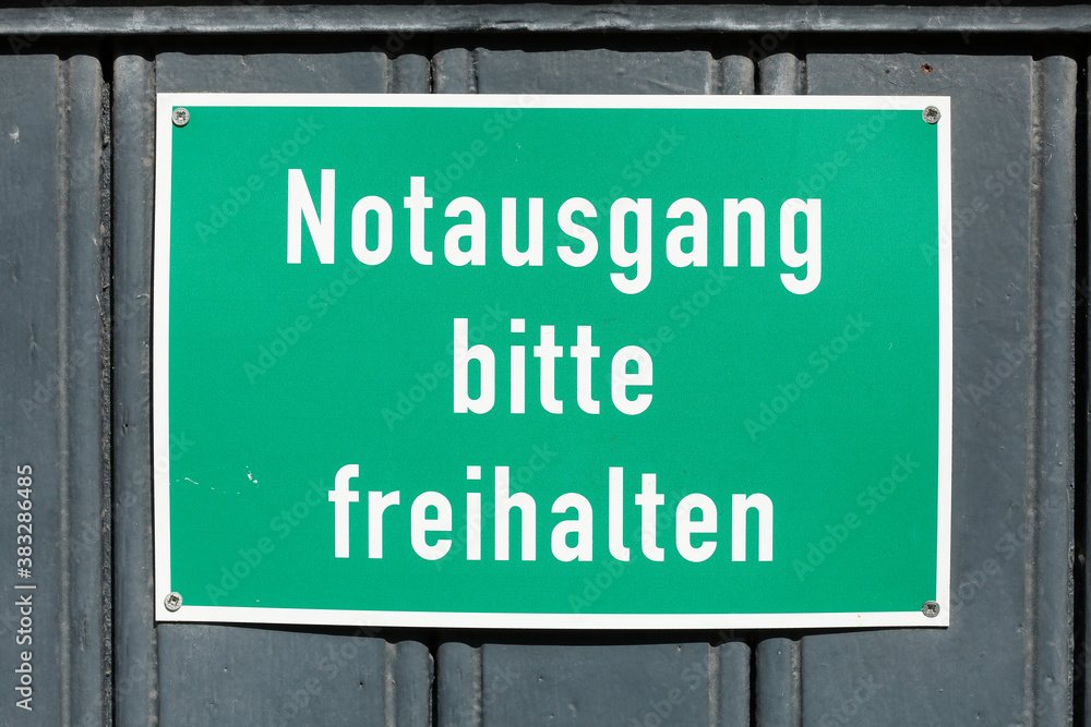 Grünes Schild Notausgang bitte freihalten an einer dunklen Holztür,  Deutschland