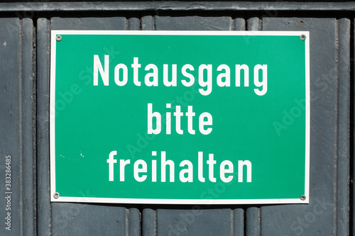 Grünes Schild Notausgang bitte freihalten an einer dunklen Holztür, Deutschland