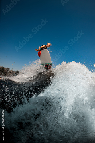 view of man jumping on the board above the splashing wave