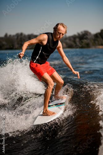 athletic man rides down the wave on surf style wakeboard on sunny day © fesenko