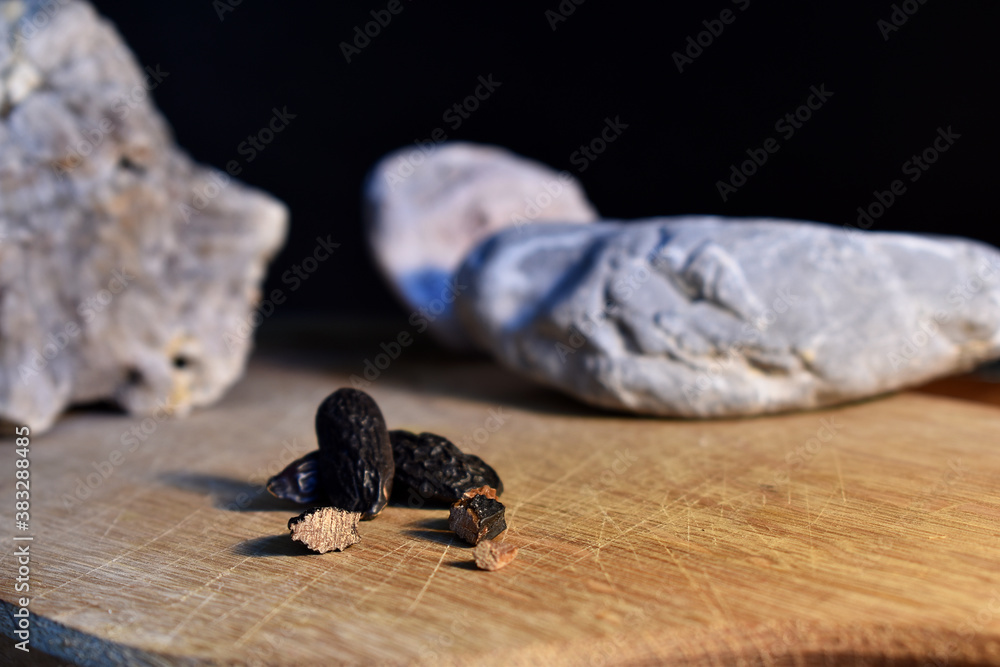Tonkabohne ganz und aufgeschnitten auf Holzbrett vor schwarzem Hintergrund mit Natursteinen, Tonka Gewürz für die Küche