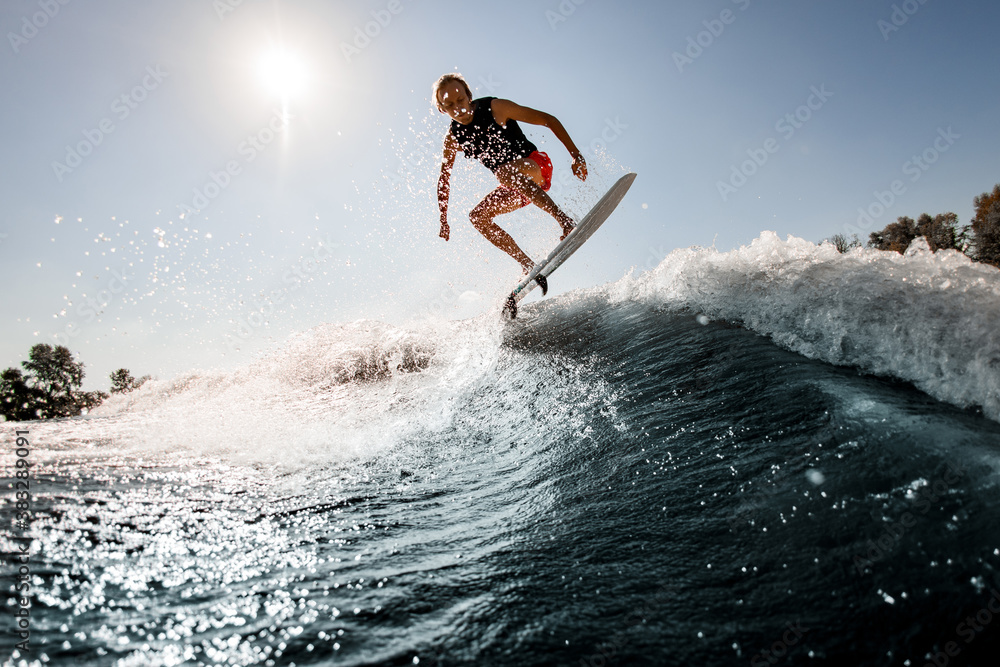 view of man jumping over river wave on board against sunny blue sky.