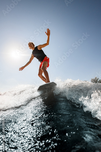 handsome man rides down the wave on surf style wakeboard on sunny day