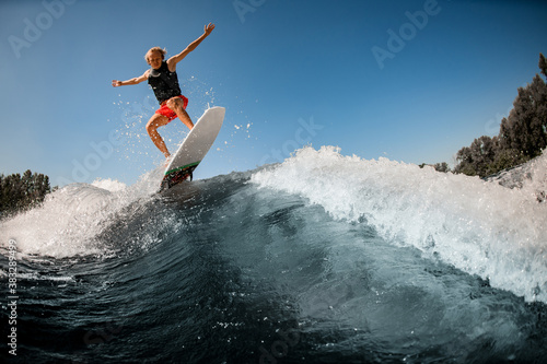 great view of man jumping over river wave on board against sunny blue sky.