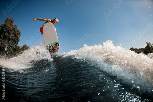 Energetic man jumping high on wave on surf style wakeboard