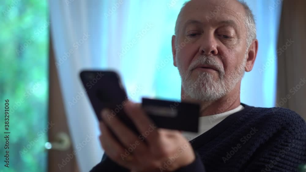 Extreme closeup of mature man using credit card to make purchase on smartphone online, typing in account number, with glass of wine. Extreme closeup of mature man using credit card to make purchase on smartphone online, typing in account number, with glass of wine.