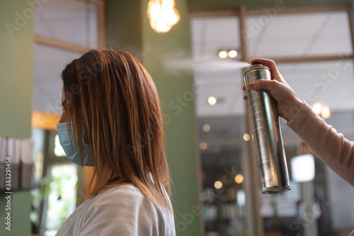 Mid section of female hairdresser spraying hairspray on hair of female customer at hair salon photo