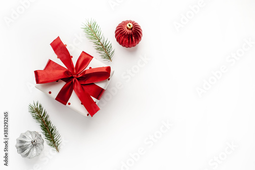 Christmas composition on a white background with a white gift box, with a red ribbon with fir branches, toys, copy space for your congratulations © александр таланцев