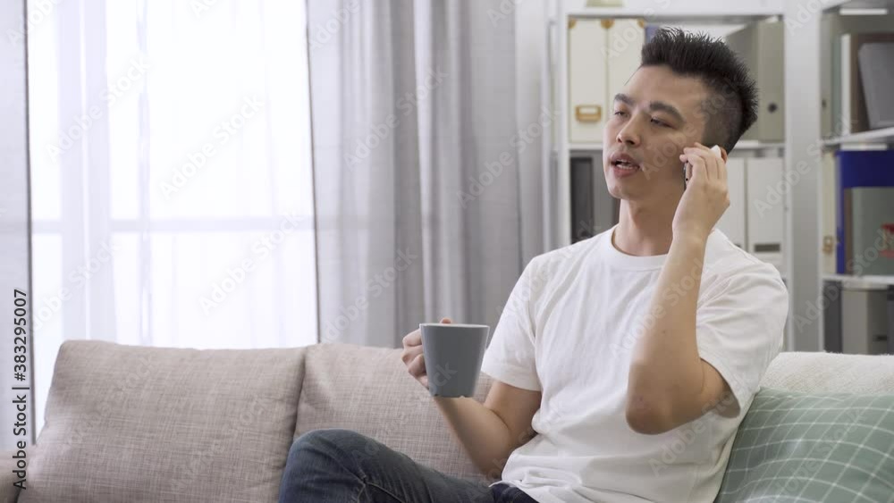 male freelancer holding coffee and smartphone is talking with his clients, nodding head showing understanding at bright home interior male freelancer holding coffee and smartphone is talking with his clients, nodding head showing understanding at bright home interior
