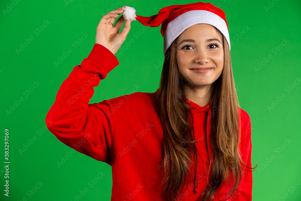 Brunette woman in santa hat and red pullover smiling, looking to the camera on isolated over green background Brunette woman in santa hat and red pullover smiling, looking to the camera on isolated over green background