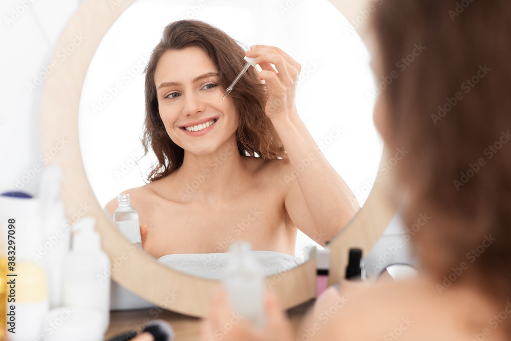 Attractive smiling young woman applying face serum Attractive smiling young woman applying face serum