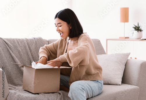 Slika na platnu Happy asian woman unpacking parcel after online shopping