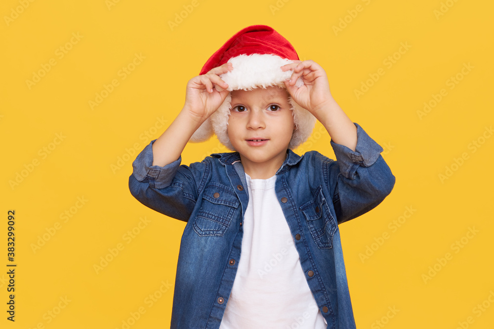 Portrait of a satisfied little child boy dressed in christmas Santa hat. laughing isolated over colored yellow background. Wow face. Season of discounts Portrait of a satisfied little child boy dressed in christmas Santa hat. laughing isolated over colored yellow background. Wow face. Season of discounts