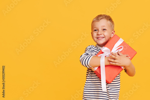 Studio shot of happy child boy celebrating holiday, unpacking gift box with excited face, posing over yellow background