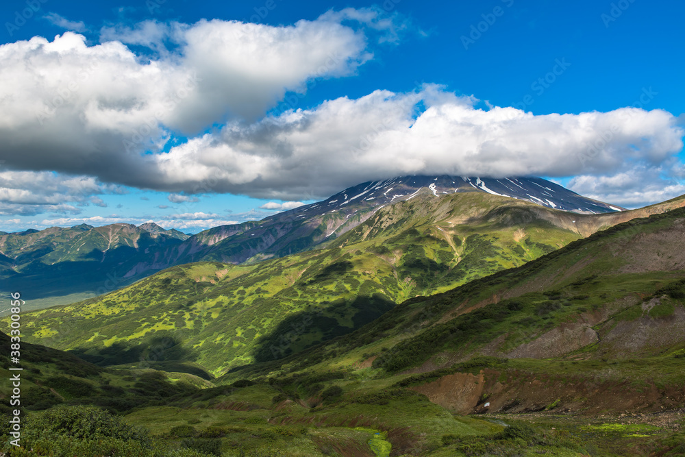 Panoramic view of the mountain valley with cloud shadows on the slopes. The top of the volcano is covered by a cloud