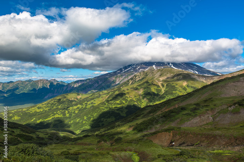 Panoramic view of the mountain valley with cloud shadows on the slopes. The top of the volcano is covered by a cloud