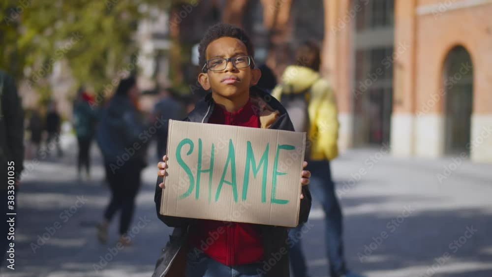 Portrait african schoolboy standing near school building and holding cardboard sign with shame text Portrait african schoolboy standing near school building and holding cardboard sign with shame text