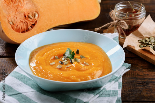 pumpkin cream soup in blue plate with pumpkin seeds on wooden background, seasonal autumn dish