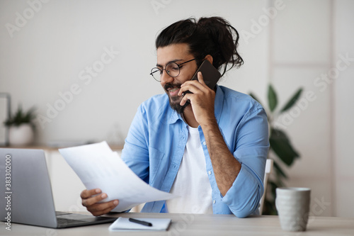 Indian Freelancer Guy Talking On Cellphone And Working With Papers At Office © Prostock-studio