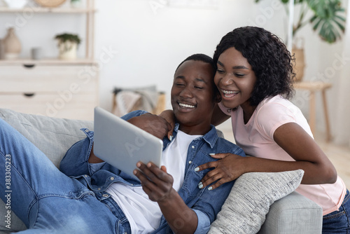 Cheerful black couple using digital tablet at home