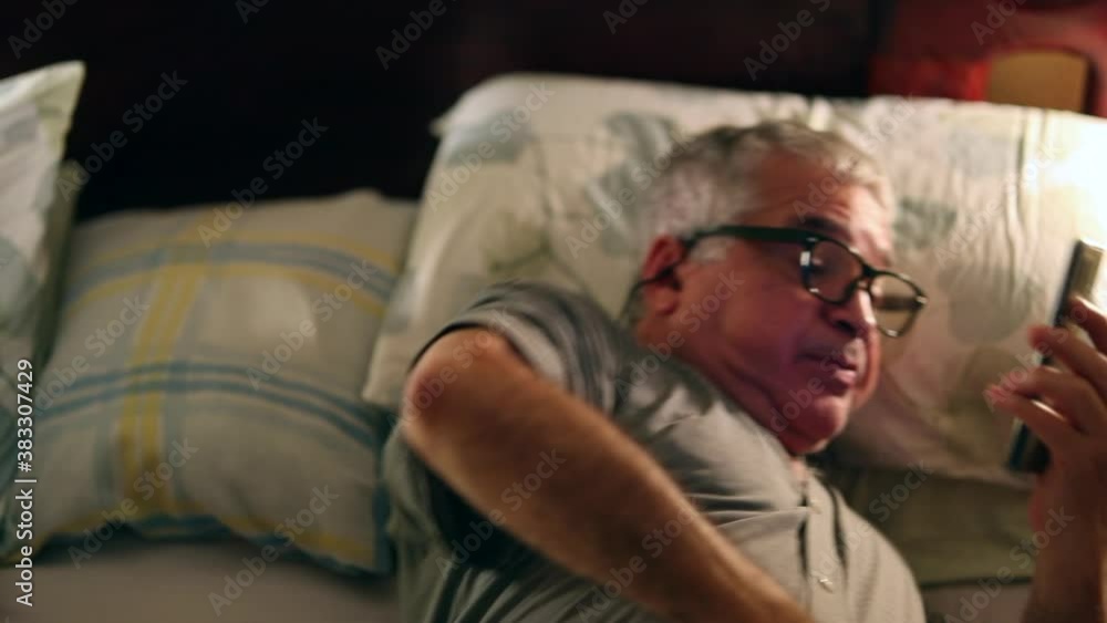 Older man watching cellphone screen at night in bed Older man watching cellphone screen at night in bed