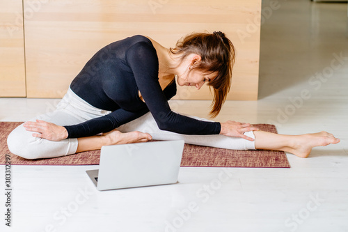 Fitness virtual online exercise. Woman Stretching from internet at home. A sporty girl in sportswear working out. Workout training in living room. Young woman laptop and foam roller a side