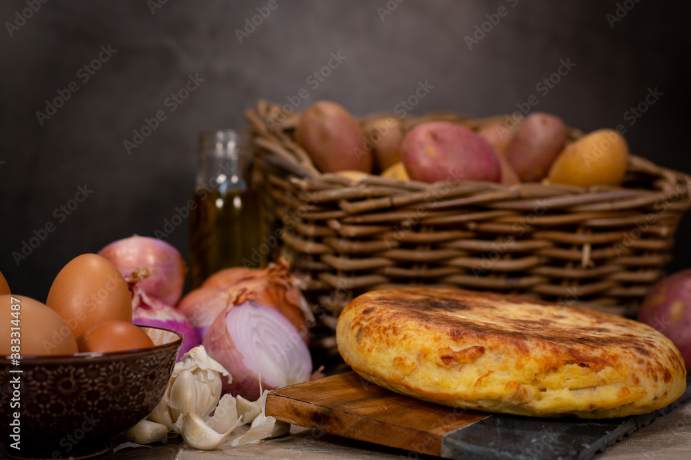 Typical Spanish potato omelette, served at the table with the necessary ingredients for the recipe, potatoes, eggs, onion and garlic Typical Spanish potato omelette, served at the table with the necessary ingredients for the recipe, potatoes, eggs, onion and garlic
