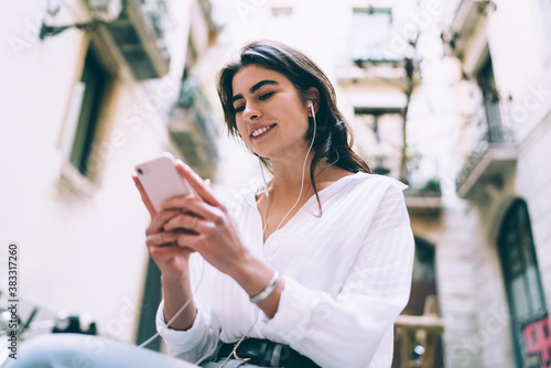 Happy woman in earphones with smartphone on street