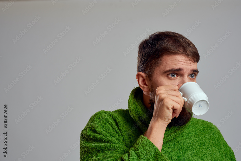 Man in a green robe with a cup of drink in his hands on a gray background cropped view Man in a green robe with a cup of drink in his hands on a gray background cropped view