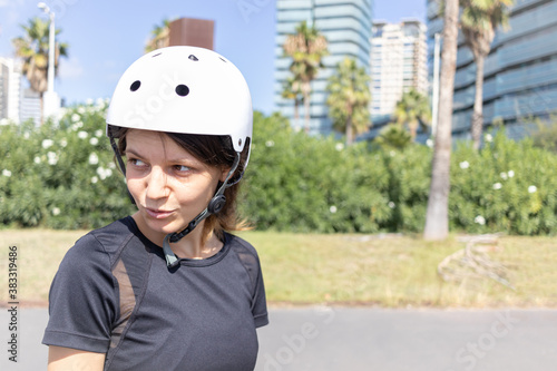 Young roller skater caucasian woman in the white helmet and black sporty clothes on a sunny day in the skatepark, urban environment © Belogorodov