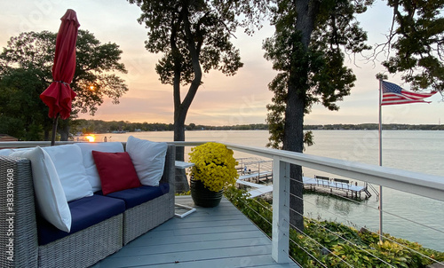 Canvas-taulu lakeside sunset on patio deck with red white blue furniture yellow mums flowers