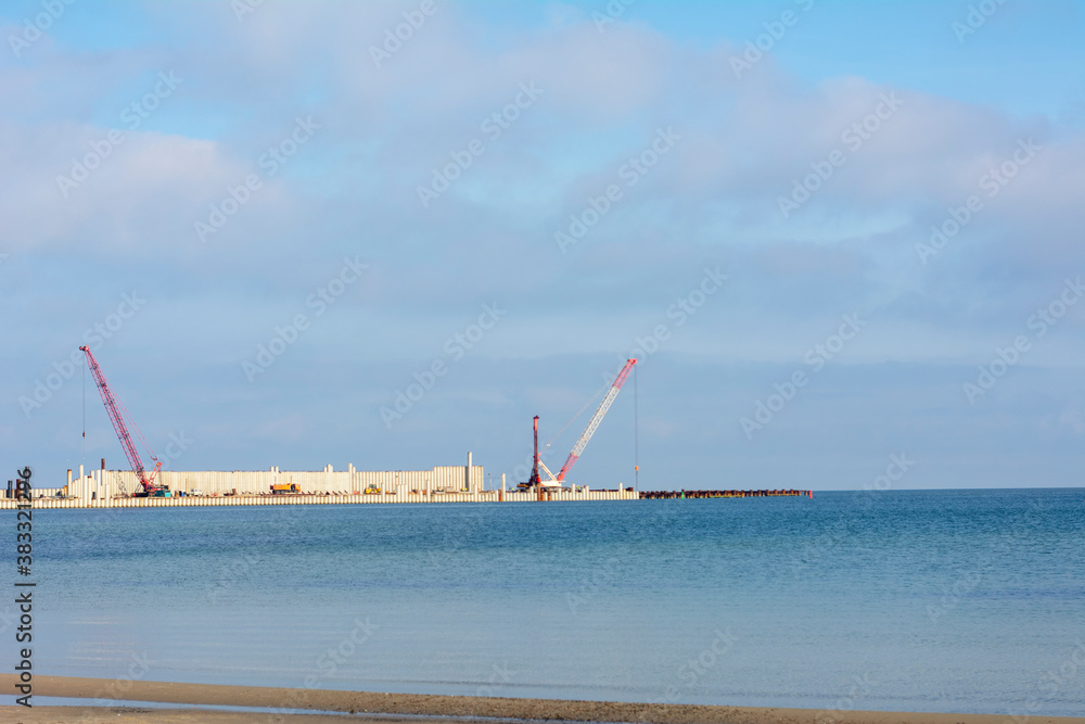 Construction of a new pier at sea. Construction machinery in the distance against the background of water and sky
