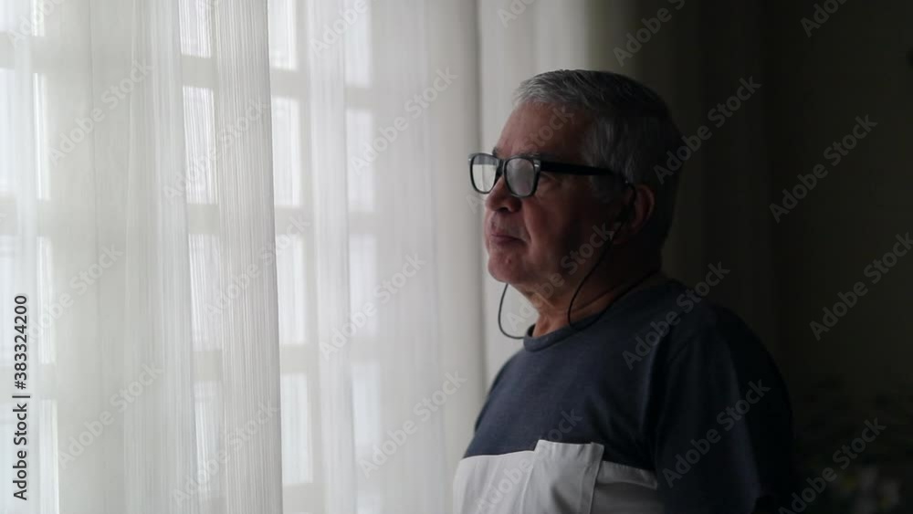 Preoccupied senior man standing by window waiting anxiously Preoccupied senior man standing by window waiting anxiously