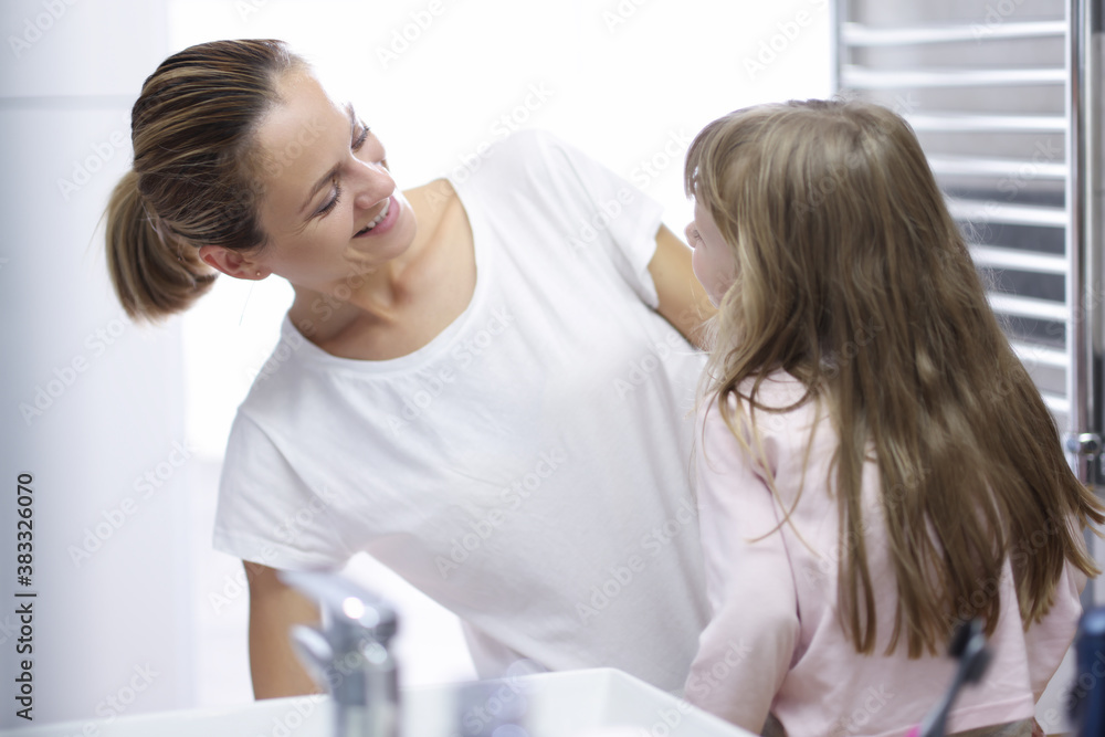 Young woman mother looking at baby and smiling in bathroom portrait. Daily morning hygiene procedures for children concept.
