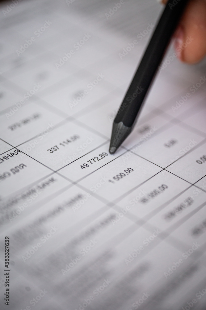 A hand checks part of a financial document A hand checks part of a financial document