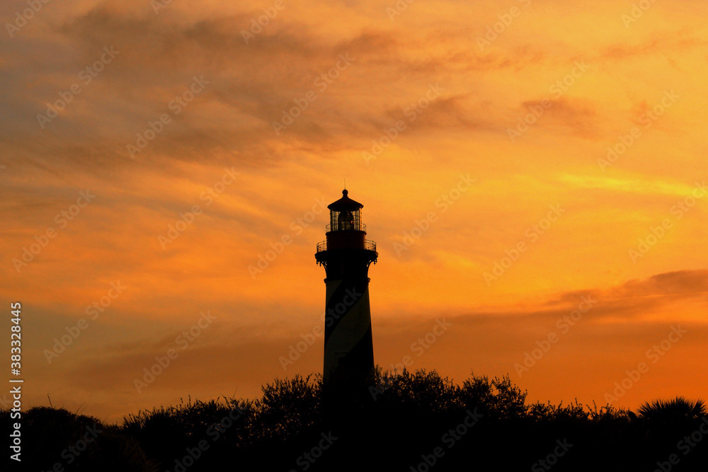 Silhouetted lighthouse at dramatic, warm, vivid, fiery  yellow and orange sunset at twilight in St. Augustine, Florida.