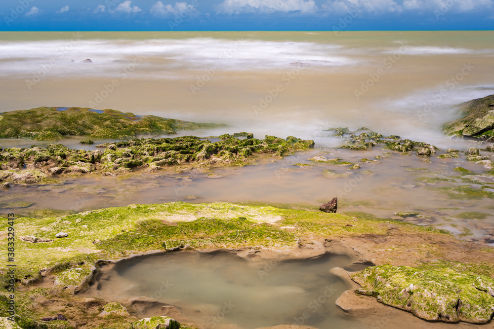 Blurred ocean over reefs with algae and under blue sky charged with nimbus clouds. Blurred ocean over reefs with algae and under blue sky charged with nimbus clouds.