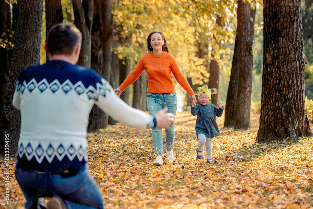 Fototapeta premium Smiling young family running into leaves on an autumns day. active games