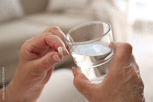 Senior woman with glass of water taking pill at home, closeup