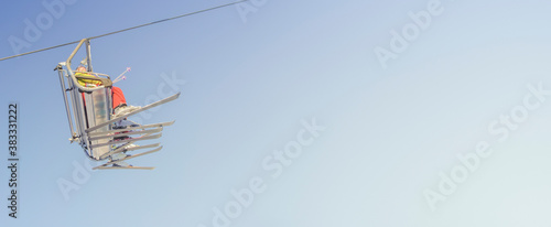Banner with big group of skiers in ski lift, going uphill in a ski resort at blue and yellow clean gradient sky during sunset with copy space for text.