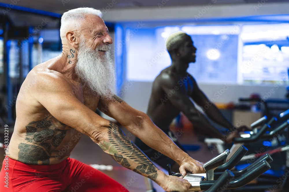 Senior and young men doing bike exercises in gym People with different age and race training on cycling machine in health wellness center Sport activity and fitness lifestyle concept Photos