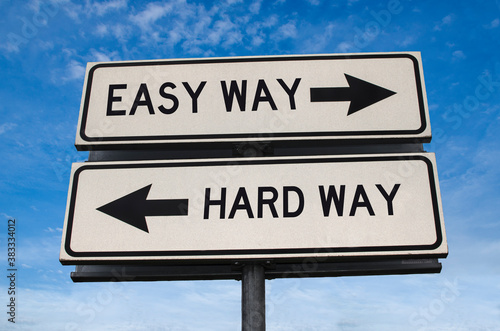 Easy way versus hard way road sign. White two street signs with arrow on metal pole with word. Directional road. Crossroads Road Sign, Two Arrow. Blue sky background. Two way road sign with text.