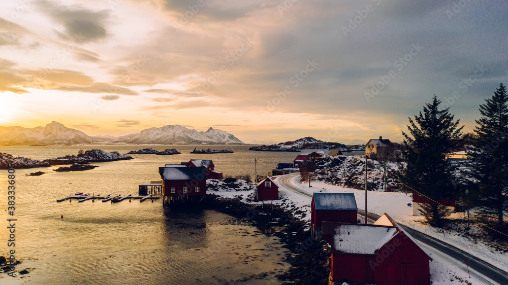 Breathtaking bird's eye view of Lofoten archipelago covered with snow surrounded by Norway sea water. Aerial view from drone of small fishing bay with pier at golden sunset light