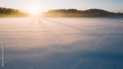 Aerial view from drone of frozen lake covered with ice and snow in winter  bird   s eye view of cold wilderness destination with beautiful scenery nature landscape at golden sunset