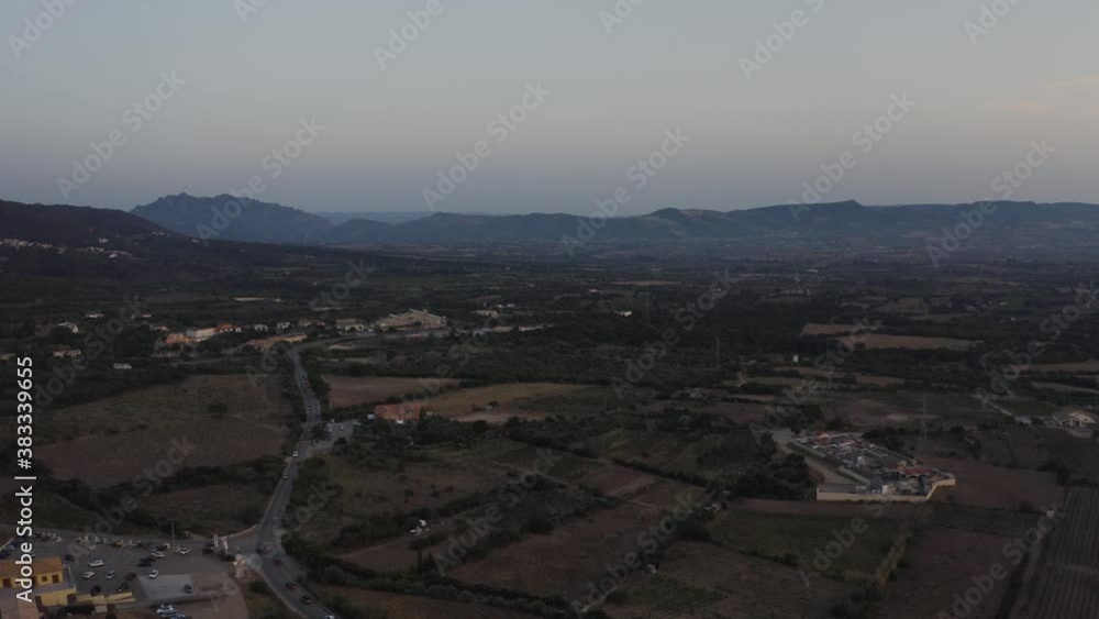 Aerial panoramic shot panning 360 degree showing city with buildings and green lands and mountains in front of the sea during sunset with cloudy sky