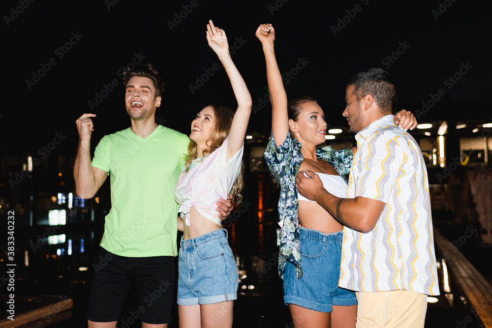 Obraz premium Young friends dancing and hugging near swimming pool at night