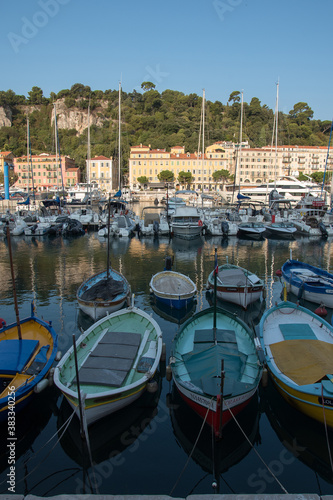 bateaux de p  cheurs dans un port au premier plan  et bateaux plus yachts au fond  devant des immeuble et une colline 