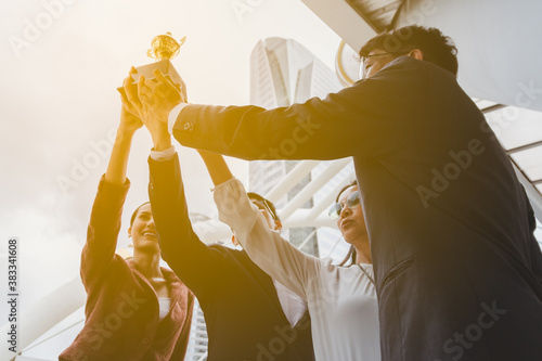 Team success of asian young businessman and businesswoman raise up the trophy and celebrate . Teamwork of successful outdoors. together.