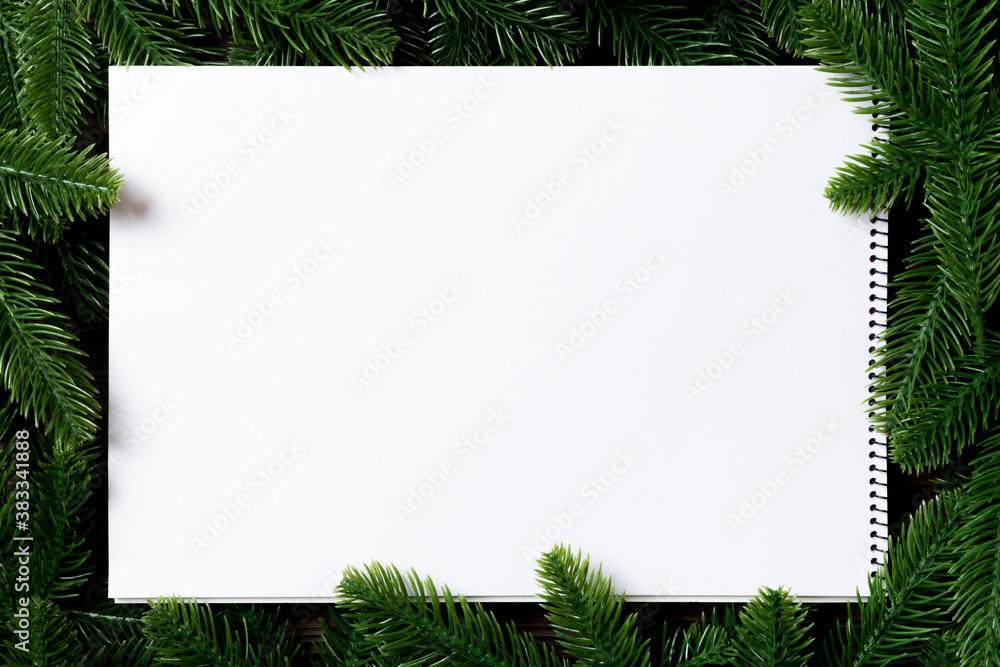 Obraz premium Top view of notebook decorated with a frame made of fir tree on wooden background. New Year time concept